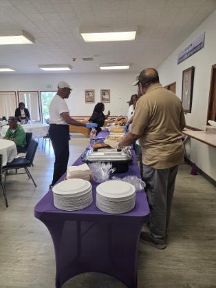 Church members serving guests at the purple-draped buffet table — MLK Memorial Baptist Church BBQ 2026