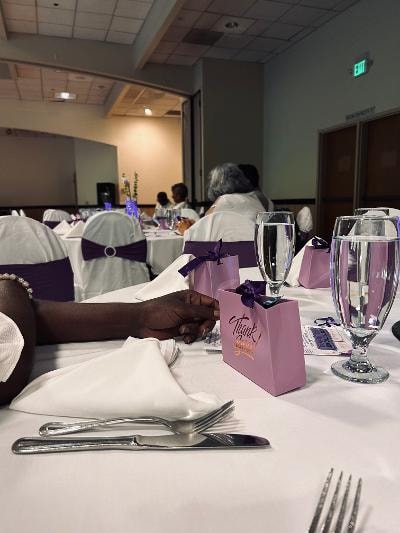 Elegant table setting with white napkins, crystal glasses, silverware, and purple Thank You gift bags at the Golden Jubilee All-White Affair — MLK Memorial Baptist Church 2026