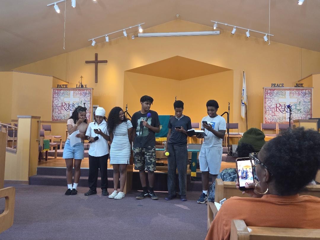 Kassie leading youth at the podium in the sanctuary — VBS Day 3 Assembly, MLK Memorial Baptist Church