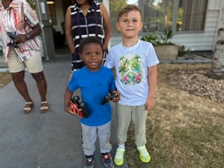 Two boys posing with toy cars outside — VBS Day 3 Assembly