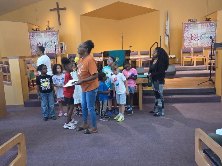 Kim and children gathered at the front of the sanctuary — VBS Day 3 Assembly