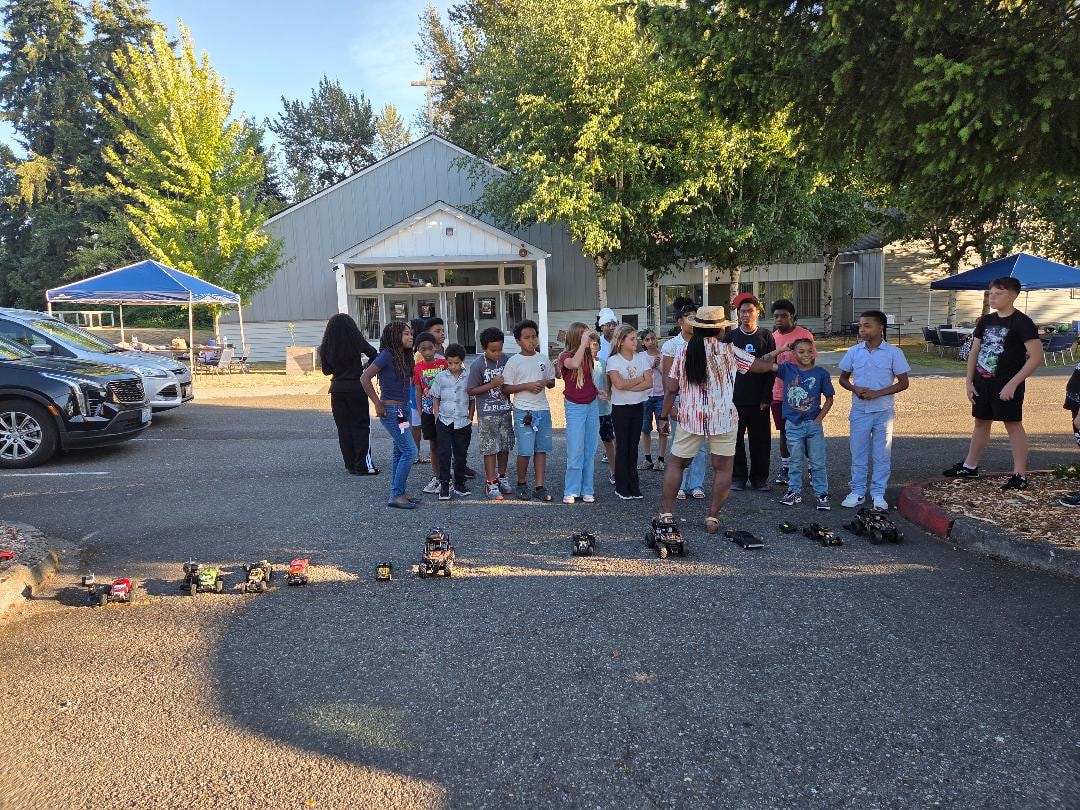 Children gathered around RC cars in church parking lot — VBS Day 3 Assembly