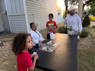 Family gathered around outdoor table with food — VBS Day 3 Assembly